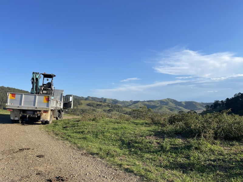Truck carrying a mini excavator on a gravel road with green hills behind