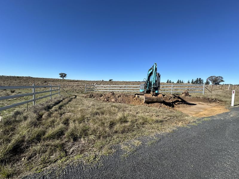 Step 1: Mini excavator digging out a rural driveway entrance off a sealed road, between new steel fence panels
