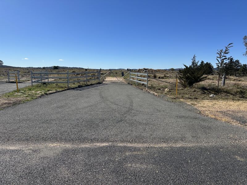 Finished bitumen seal on a wide rural driveway entrance with steel gates and fence panels