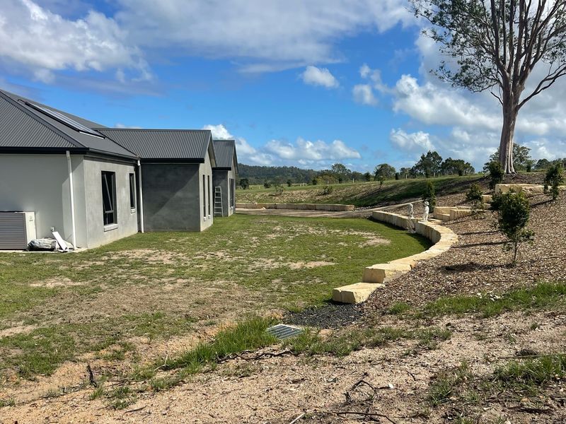 Finished house site with a levelled yard, curved sandstone block retaining wall and a drainage pit