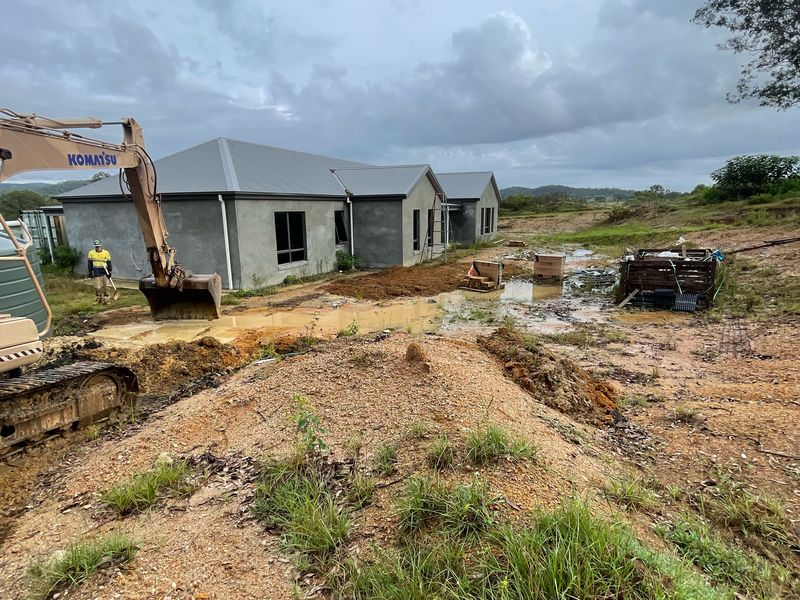 Komatsu PC130 excavator working on a wet house site beside a new home